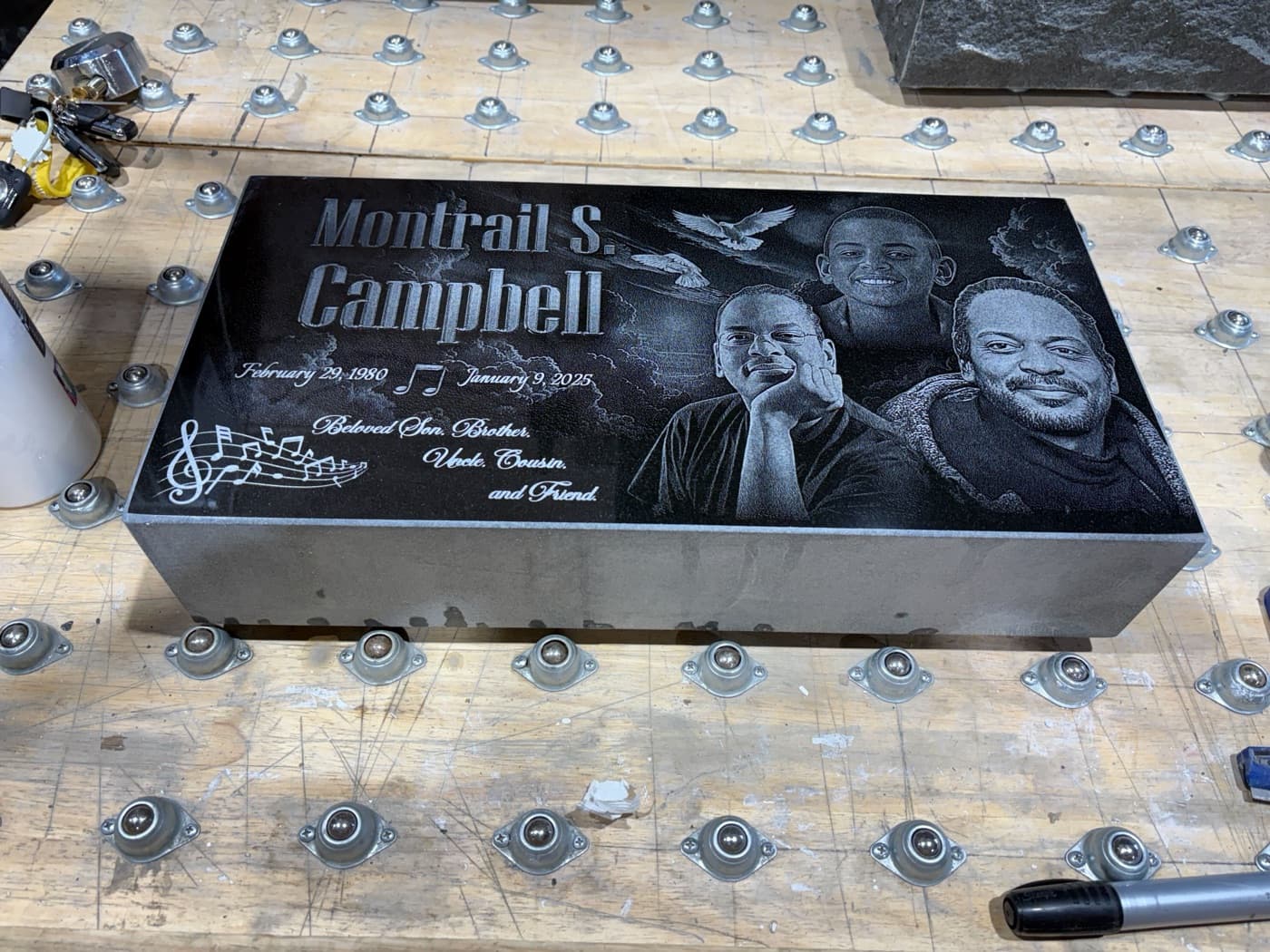 Black granite bevel marker for Montrail S. Campbell — triple laser-engraved portrait group with music notes and cloud scene on the angled face