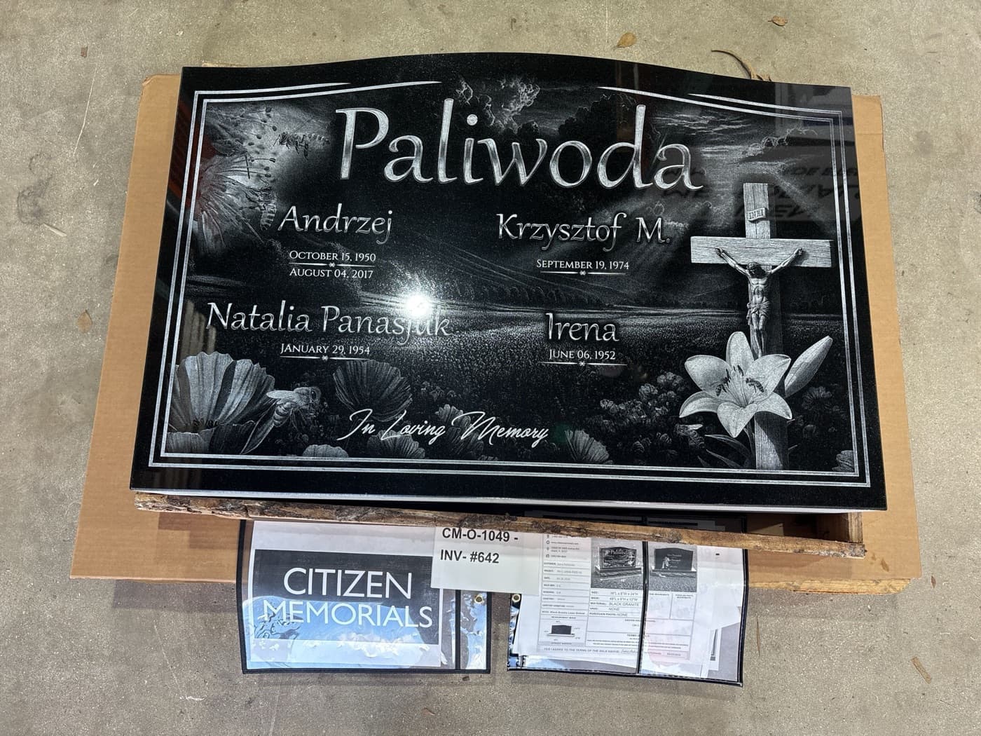 Large companion flat marker for the Paliwoda family — four names, crucifix, and scenic floral and butterfly engraving spanning the full stone width
