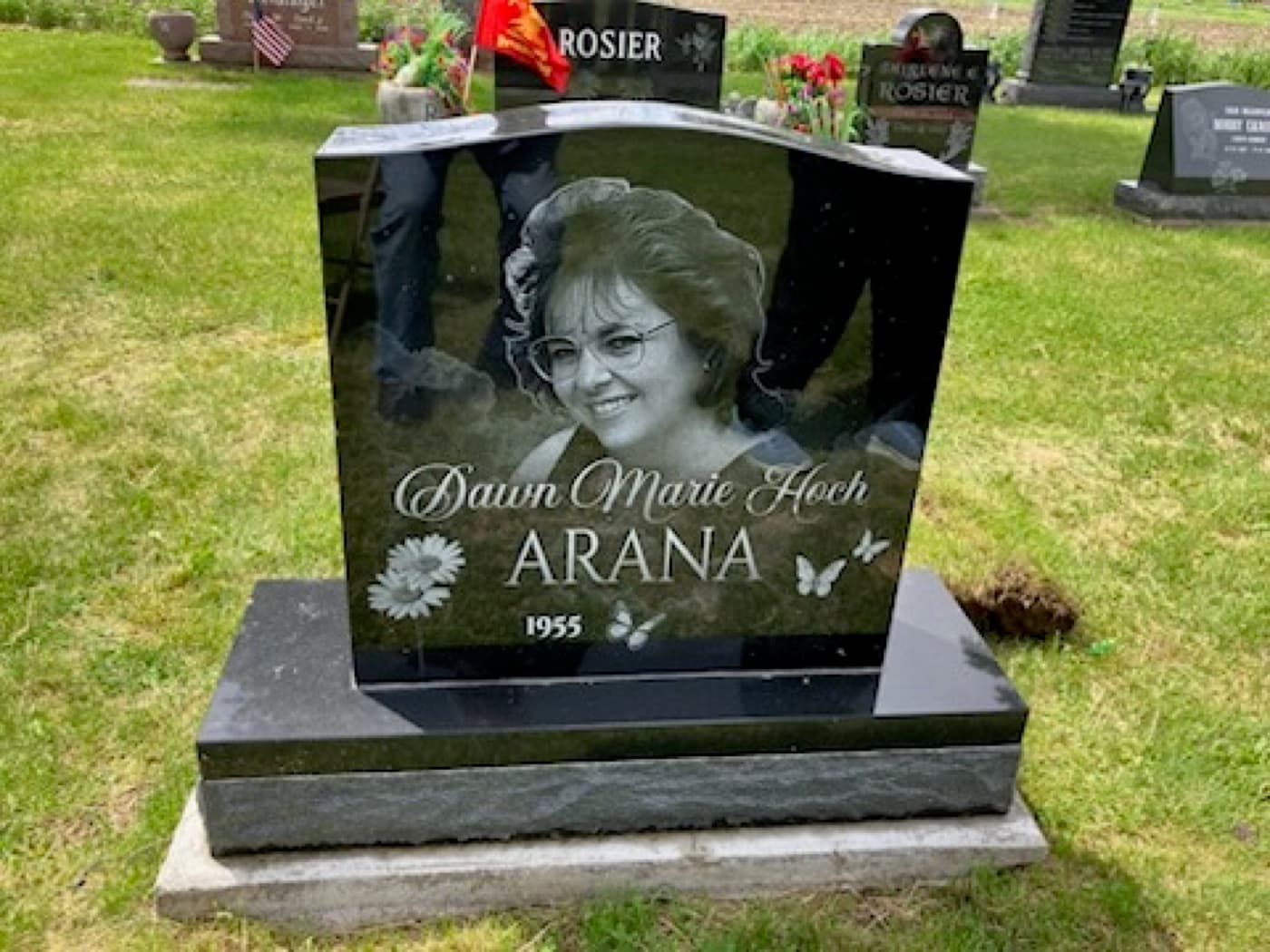 Upright headstone for Dawn Marie Hoch Arana installed in a cemetery — full-face laser-engraved portrait surrounded by daisy and butterfly engravings